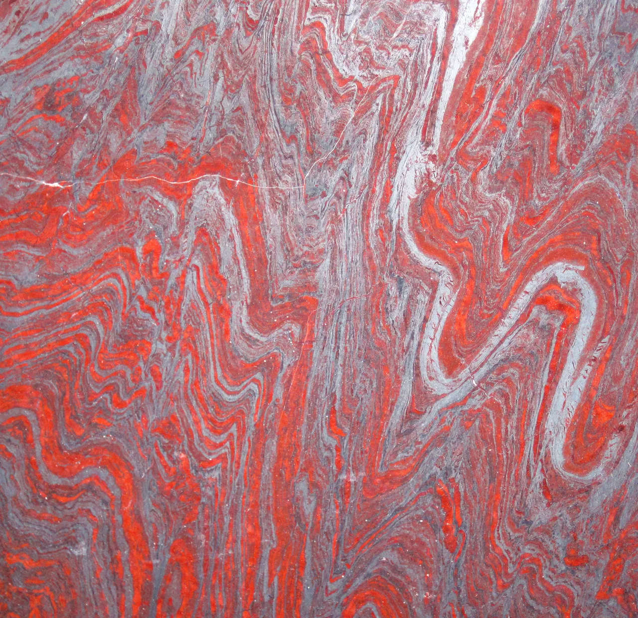Hollywood Granite - jaspilite meta-BIF (locally called itabirite) from the Paleoproterozoic-aged Minas Supergroup in the Iron Quadrangle District in Minas Gerais State, Brazil. BIFs in the Iron Quadrangle have long been mined as a source of iron ore. Recently, BIFs there have been quarried as a source of attractive, high-priced, and very-heavy-for-their-size decorative stones.
Banded iron formations, or BIFs, are extinct, marine sedimentary rocks (most have been well metamorphosed) that usually consist of alternating reddish- and silvery-gray iron-rich layers. They are most common in the Paleoproterozoic rock record (2.5 to 1.6 Ga). They represent a time when Earth’s oceans “rusted out” as small amounts of atmospheric free oxygen (O2 gas) combined with dissolved iron in seawater to precipitate as iron oxide minerals. Some workers hypothesize that bacterial mats on the seafloor mediated the precipitation of iron oxides.
Many specific varities of BIFs exist, including jaspilite, taconite, quartzite-specularites, magnetitites, etc.