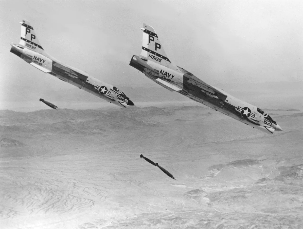 Two U.S. Navy Vought F-8J Crusaders (BuNo 149155, 150317) of Photographic Reconnaissance Squadron VFP-63 drop Mk 82 227 kg bombs in the Chocolate Mountain Aerial Gunnery Range, California (USA). VFP-63 used the F-8J only for training as it regularly flew the RF-8G reconnaissance version.