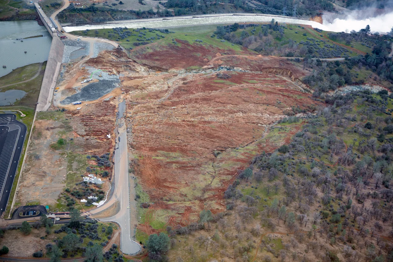 Aerial view of damage to the Oroville Dam during the 2017 Oroville Dam crisis, with erosion caused during use of the emergency spillway in the middle of the image and the crater in the main spillway in the upper left corner