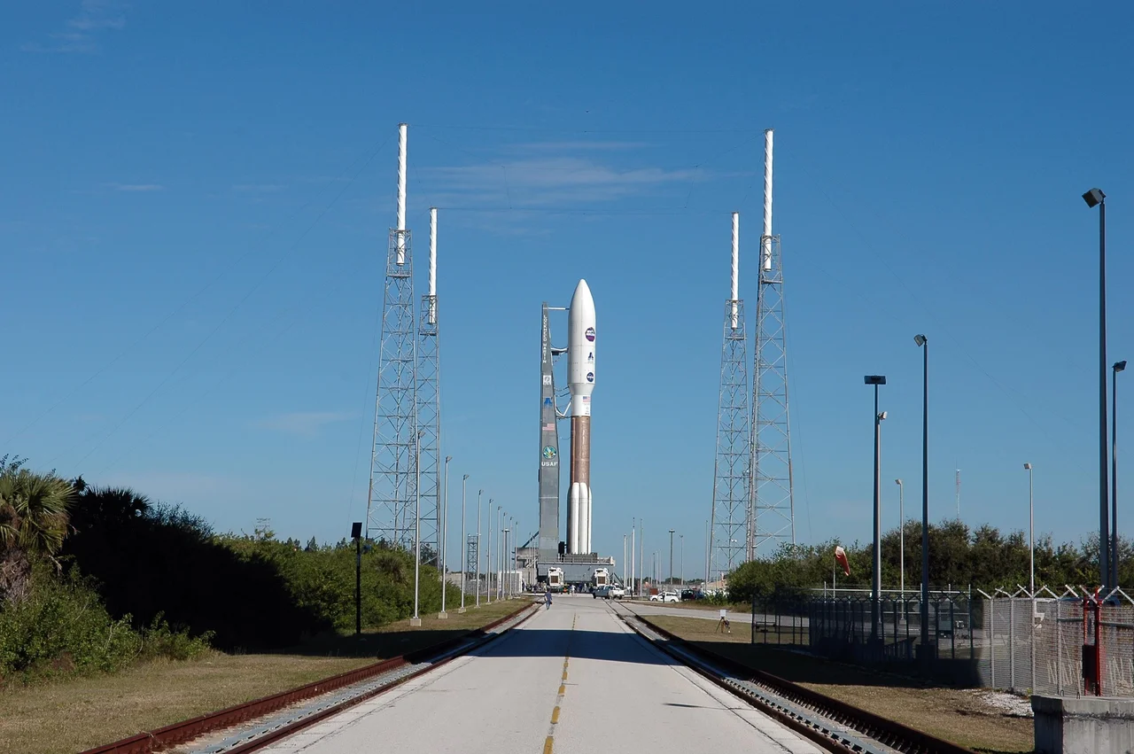 On Complex 41 at Cape Canaveral Air Force Station, the Atlas V expendable launch vehicle with the New Horizons spacecraft has been moved to the pad. Umbilicals have been attached.  Seen near the rocket are lightning masts that support the catenary wire used to provide lightning protection.  Liftoff is scheduled for 1:24 p.m. EST Jan. 17.  After its launch aboard the Atlas V, the compact, 1,050-pound piano-sized probe will get a boost from a kick-stage solid propellant motor for its journey to Pluto. New Horizons will be the fastest spacecraft ever launched, reaching lunar orbit distance in just nine hours and passing Jupiter 13 months later. The New Horizons science payload, developed under direction of Southwest Research Institute, includes imaging infrared and ultraviolet spectrometers, a multi-color camera, a long-range telescopic camera, two particle spectrometers, a space-dust detector and a radio science experiment. The dust counter was designed and built by students at the University of Colorado, Boulder. A launch before Feb. 3 allows New Horizons to fly past Jupiter in early 2007 and use the planet’s gravity as a slingshot toward Pluto. The Jupiter flyby trims the trip to Pluto by as many as five years and provides opportunities to test the spacecraft’s instruments and flyby capabilities on the Jupiter system. New Horizons could reach the Pluto system as early as mid-2015, conducting a five-month-long study possible only from the close-up vantage of a spacecraft.