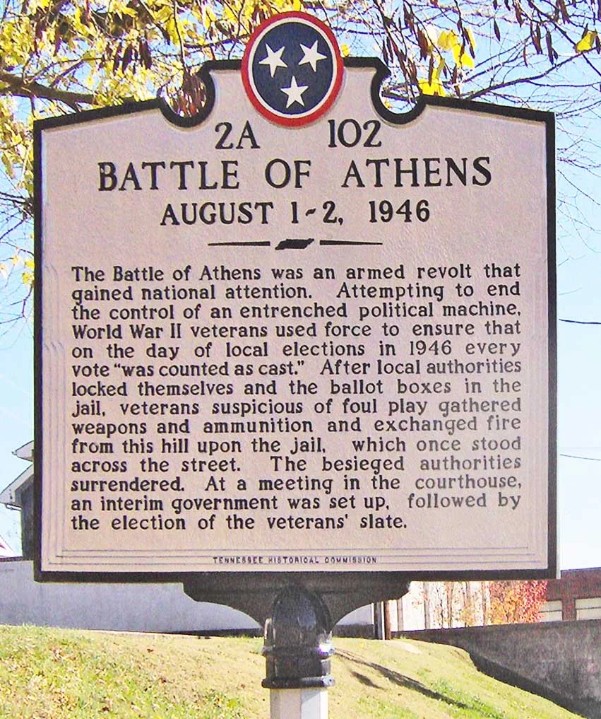Tennessee Historical Commission marker in Athens, Tennessee, in the southeastern United States.  The marker recalls the "Battle of Athens," which occurred on August 2, 1946, when local officials locked themselves in the old jail (formerly off-camera to the right), allegedly to fix election results.  An armed group of World War II veterans and supporters assembled on the hill to the left and exchanged fire with the authorities in the jail.