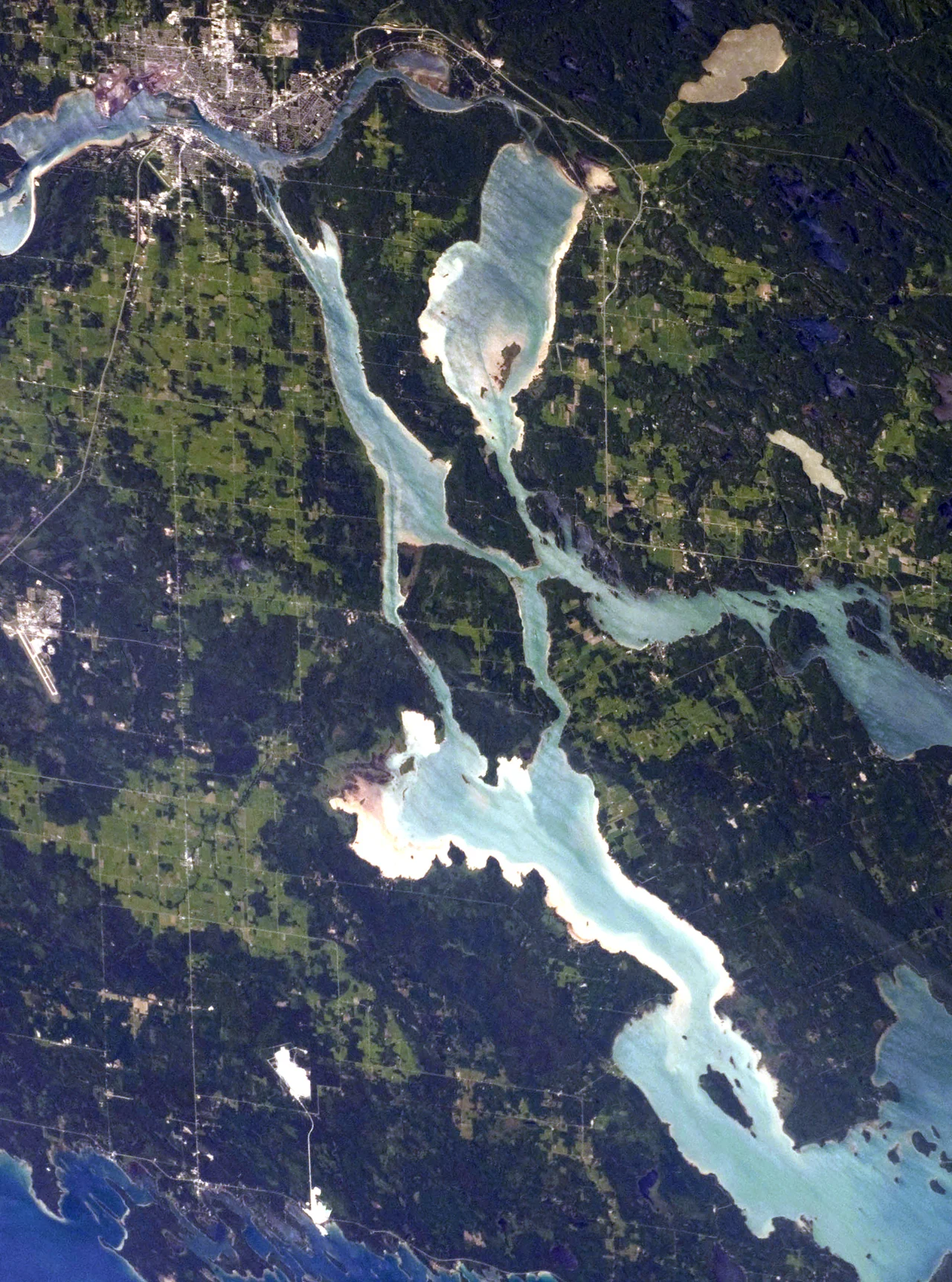 Centred in this astronaut photograph is Neebish Island, Michigan.  To the north of it is Sugar Island, Michigan. To the east is St. Joseph Island, Ontario. To the west and south is the eastern corner of Michigan's upper peninsula. The twin cities of Sault Ste Marie, Ontario and Michigan can be seen in the upper right hand corner.  These are located across the St. Marys River, which forms part of the international boundary between Canada (Province of Ontario) and the United States (State of Michigan). These urban areas have a distinctive gray to white colour, contrasting with the deep green of forested areas in Ontario and the lighter green of agricultural fields in Michigan. The water surfaces in the lakes and rivers vary from blue to blue-green to silver, likely the result of varying degrees of sediment and sunglint—light reflecting from the water surface back to the International Space Station.