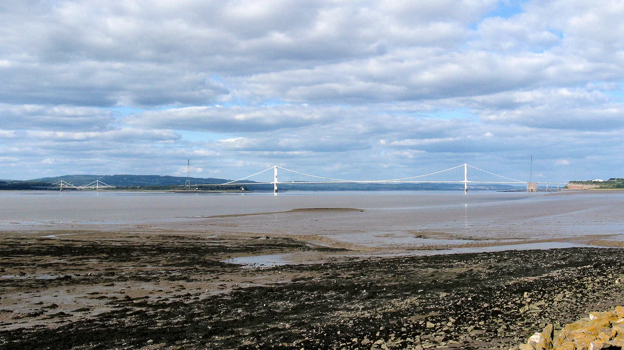 On the right the Severn Bridge crosses the River Severn. On the left the much smaller Wye Bridge spans the River Wye.
The Severn bridge is entirely in England - the right-hand tower is in South Gloucestershire and the other tower is in Gloucestershire.
The right-hand half of the Wye bridge is also in England (Gloucestershire). Wales starts halfway between its towers (Monmouthshire).