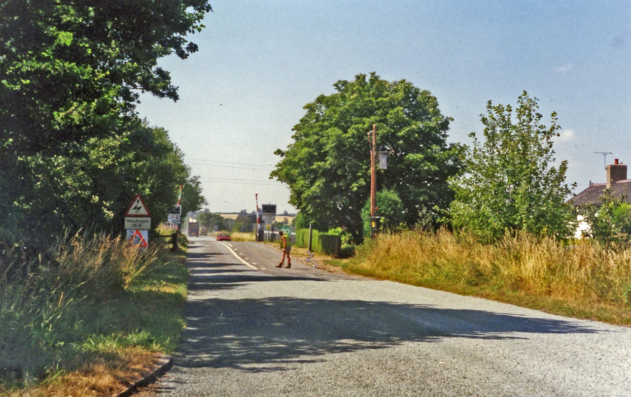 Approaching crossing at site of Hixon station, 1995
View westward, the station (unstaffed Halt since 20/7/31, closed 6/1/47 when local services ceased) had been on the left: ex-North Stafford Stone (to right) - Colwich (to left) loop used by London Euston - Manchester through trains running via Stoke-on-Trent and electrified in 1965-66. There was an RAF Airfield close by and the line was frequently blocked by crashing aircraft during World War Two, but the site is famous for the extraordinary accident of 6/1/68 when an express crashed into a low-loader creeping across the level-crossing carrying a 120-ton electrical transformer.
