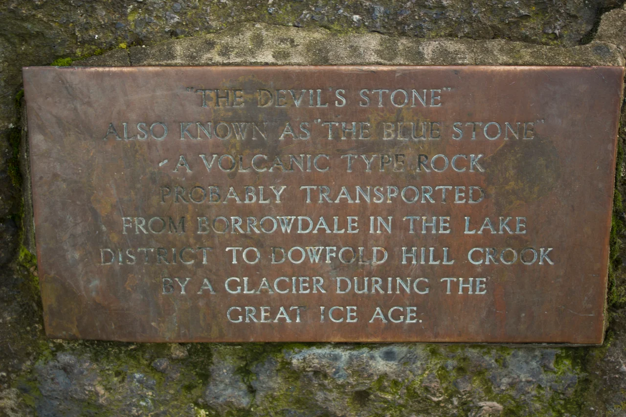 Plaque reads: ""The Devils's Stone". Also known as "The Blue Stone". A volcanic type rock probably transported from Borrowdale in the Lake District to Dowfold Hill Crook by a glacier during the Great Ice Age.