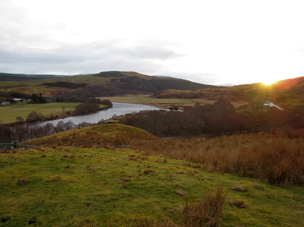 View of Strathoykel in northern Scotland looking west (upstream) from Tutim cemetery at sunset. The cemetery wall is in the foreground, Brae farm on the left of the photo, and Tuiteam house on the right. The mouth of the Tutim Burn can be seen entering the River Oykel roughly level with Tuiteam house. The hill is  Ben Chreagach. The site is notable for the en:Battle of Tuiteam Tarbhach which took place around Tuiteam house in about 1406.