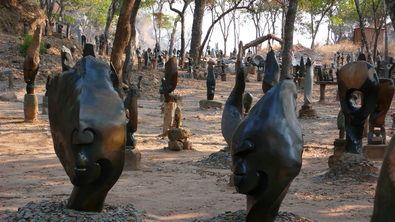 Hundreds of stone sculptures are displayed among trees at the Tengenenge Art Community in northern Zimbabwe. The photo was taken in October, during the dry season, and there is smoke in the background from burning burning fields.
