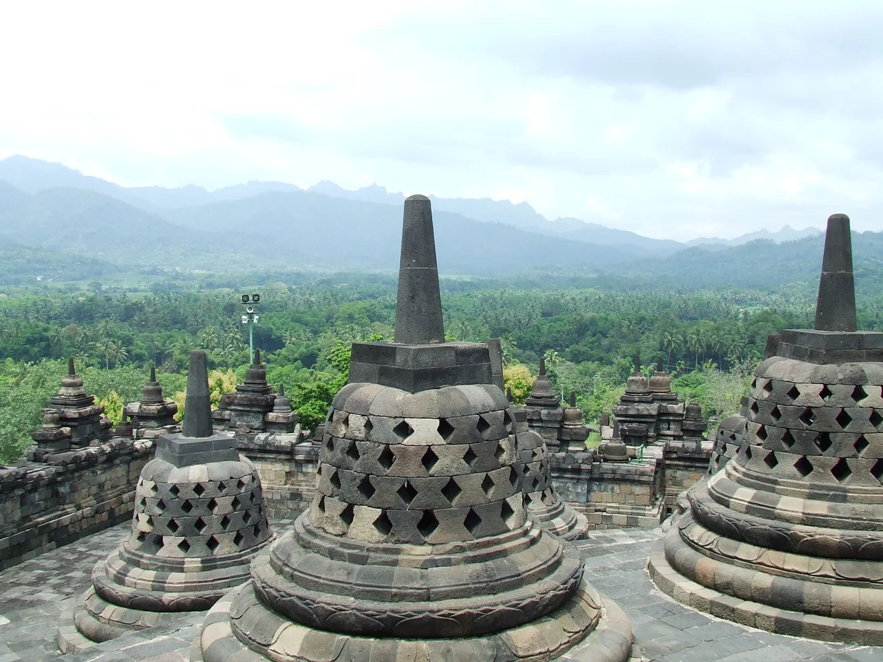 Painting title: "The Borobudur as Pilgrimage Site" (Dutch title: De Borobudur als bedevaartsoord). The painting reconstructs a scene of the Mahayana Buddhist temple in its heyday on Java island. Possibly in the 9th century during the Shailendra dynasty. Measurement: 67 x 96cm. The painter included two figures in white robes on the right which represent his grandfather (with a beard) Dr. D.A. Hooijer and his uncle Gijs Hooijer.
Signature: lower right: G.B. Hooijer (Gijsbert Brandt Hooijer). Inventory number: TM-75-2. Material: paper. Painting made with tempera paint. Made in circa 1910s (before 1919). This painting was donated to the Wereldmuseum in Amsterdam on 1 October 1919. Literature references: John N. Miksic, Noerhadi Magetsari, Jan Fontein, Timbul Haryono, Idham Bachtiar Setiadi: Borobubur Majestic, Mysterious, Magnificent (2011), p. 236. Publications: Koos van Brakel et al, Indie omlijst, vier eeuwen schilderkunst in Nederlandsch-Indie, 1998, p. 149.