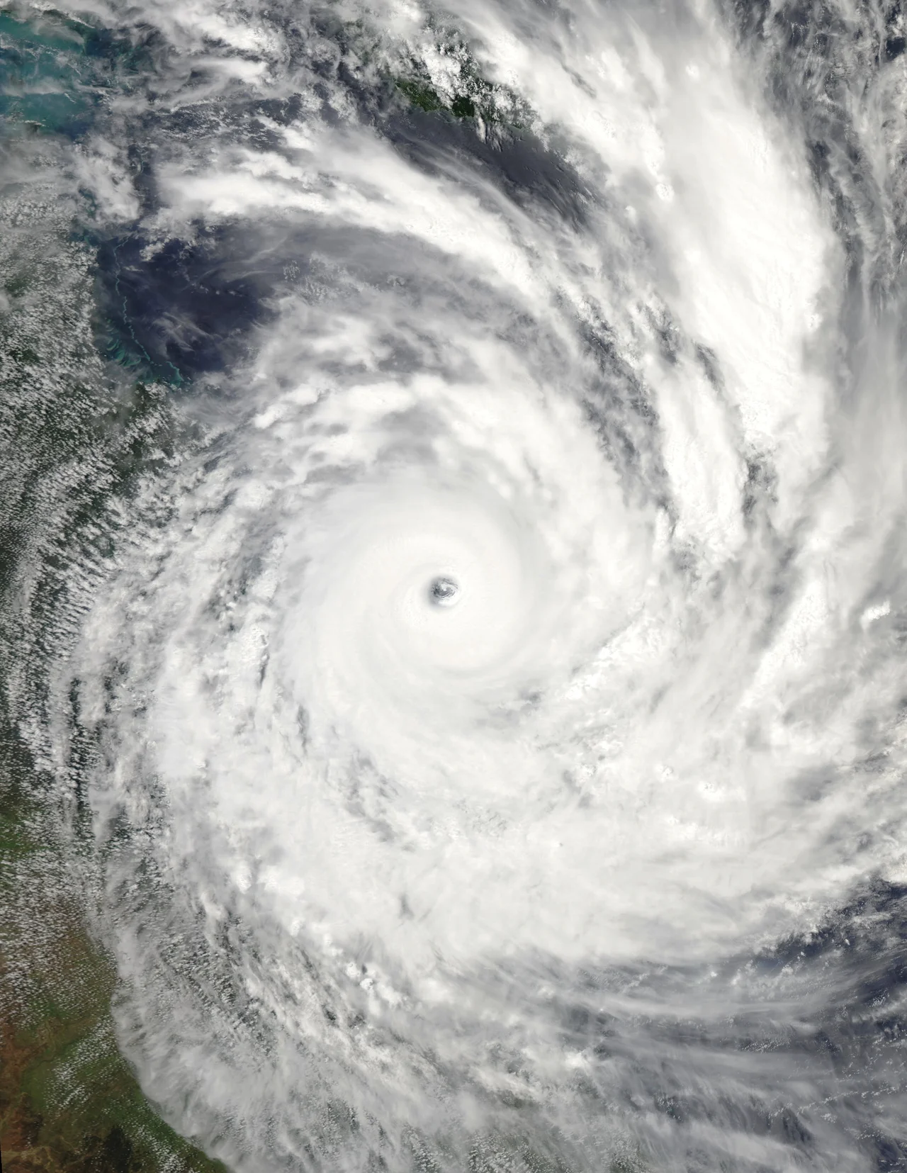 Before the year 2004, only two tropical cyclones had ever been noted in the South Atlantic Basin, and no hurricane. However, a circulation center well off the coast of southern Brazil developed tropical cyclone characteristics and continued to intensify as it moved westward. The system developed an eye and apparently reached hurricane strength on Friday, March 26, before eventually making landfall late on Saturday, March 27, 2004.
The crew of the International Space Station was notified of the cyclone and acquired excellent photographs of the storm just as it made landfall on the southern Brazilian state of Santa Catarina (the storm has been unofficially dubbed “Cyclone Catarina”). Note the clockwise circulation of Southern Hemisphere cyclones, the well-defined banding features, and the eyewall of at least a Category 1 system. The coastline is visible under the clouds in the upper left corner of the image.