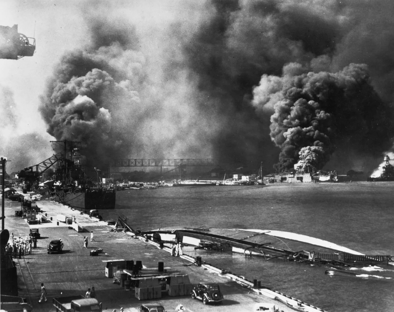 Pearl Harbor Attack, 7 December 1941: View from Pier 1010, looking toward the Pearl Harbor Navy Yard's drydocks, with the destroyer USS Shaw (DD-373) in floating drydock YFD-2 and the battleship USS Nevada (BB-36) burning at right. In the foreground is the capsized minelayler USS Oglala (CM-4), with the light cruiser USS Helena (CL-50) further down the pier, at left. Beyond Helena is Drydock No.1, with USS Pennsylvania (BB-38) and the burning destroyers USS Cassin (DD-372) and USS Downes (DD-375).