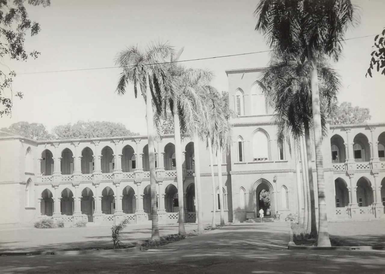 Main building of Khartoum University. A palm lane leading up to to the pointed arched entrance of a symmetrical building with galleries on two floors. "E"?