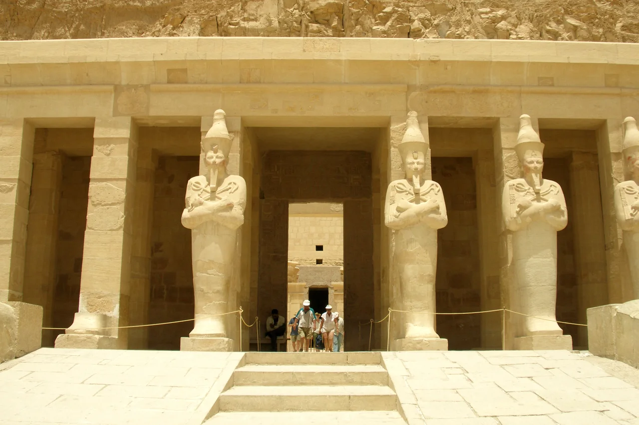 Osirian statues of Hatshepsut at her tomb. The Temple of Hatshepsut is built into a cliff face that rises sharply above it. A turning point in the megalithic geometry of the Old Kingdom. Thebes, Luxor, Egypt.