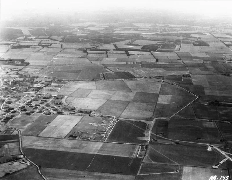 IWM caption : Oblique aerial view of RAF Feltwell, Norfolk, seen from the west, looking to the Breckland beyond. Vickers Wellingtons of Nos, 57 and 75 (New Zealand) Squadrons RAF can be seen parked in front of the hangars and on the airfield perimeter, as well as on pan-shaped hard-standings in the adjoining fields.