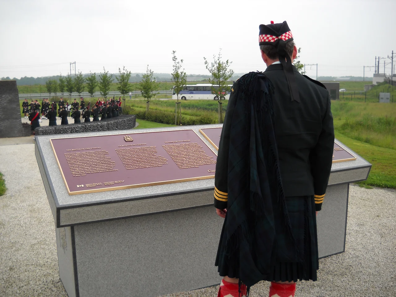 Lieutenant Colonel Mike Vernon, CD, Commanding Officer of The Calgary Highlanders, ponders the monument to the 5th Canadian Infantry Brigade erected at the site of the Walcheren Island Causeway, in memory of the sacrifice of the three Canadian regiments, as well as soldiers of the 52nd (Lowland) Division of the British Army who fought a pitched battle there beginning on Hallowe'en night 1944. The Calgary Highlanders sent a contingent to visit European battlefields in June 2010 to mark the centennial year of the regiment. In the background, the Regimental Pipes and Drums play at the site of monuments erected to the memory of Allied soldiers who fell fighting the Germans in the vicinity during the invasion of 1940.
