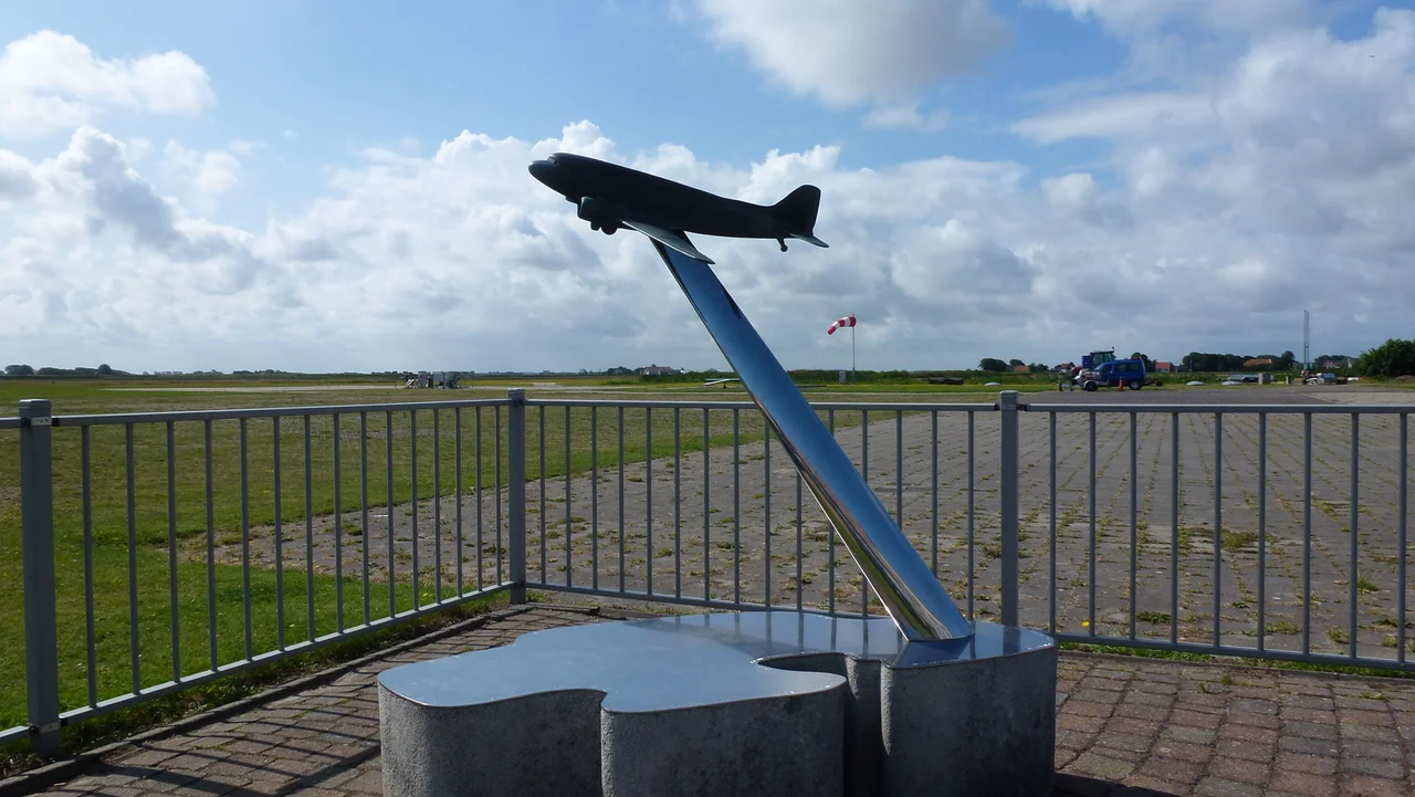 Dakotaramp Dakota monument, Texel Airport. Bronzen beeld van een DC-3 boven een in roestvast staal uitgevoerd silhouet van het eiland Texel met daarop de namen van de 32 omgekomen inzittenden. Plaquette: Ter herinnering aan de vliegramp op de Waddenzee, 25 september 1996