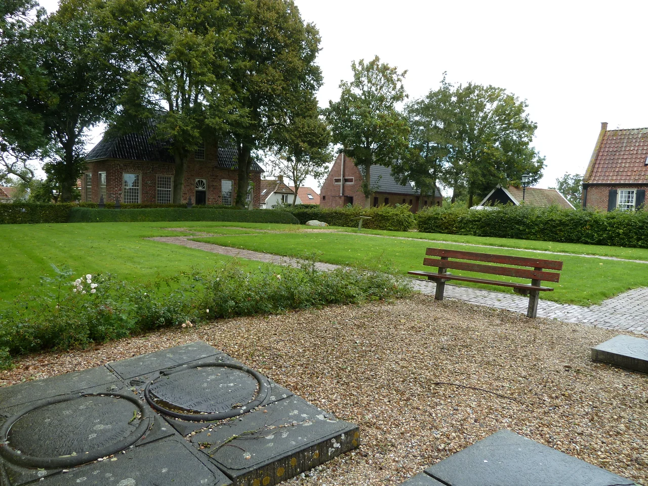 Gezicht op een deel van het kerkhof van Groot Wetsinge met links op de achtergrond de pastorie en op de voorgrond de afmetingen van de vroegere kerk van Groot Wetsinge.