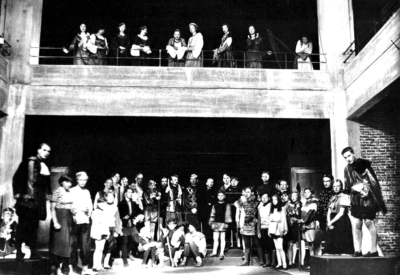 Inside view of the stage hall planned by Berlin-based renowned architect Bruno Ahrends (1878–1948) for progressive boading school Schule am Meer (School by the Sea) on the East Frisian island Juist in Prussia. Students and teachers alike are costumed on stage with its elevated pedestals to the left and to the right. Standing in the stage's center Swiss teacher Rudolf Aeschlimann (1884–1961, with a pole) and 5 positions from him to the right deputy headmaster Dr. Paul Reiner (1886–1932) from Middle Franconia in Bavaria can be recognized. The building was unique in German Reich, the only free-standing theater hall of any private or state-run school (until today).