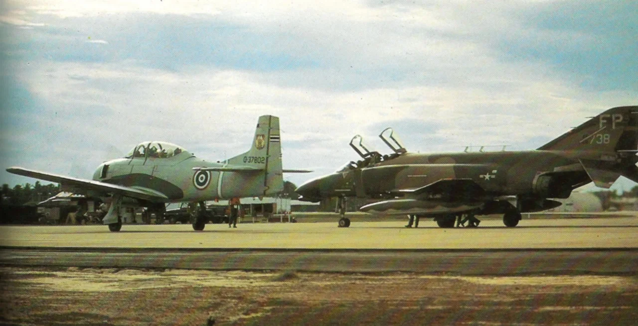 A U.S. Air Force McDonnell Douglas F-4D Phantom II (s/n 66-8738) from the 497th Tactical Fighter Squadron, 8th Tactical Fighter Wing has its weapons armed at a 'last chance' checkpoint at Ubon Royal Thai Air Force Base prior to a mission in North Vietnam in September 1972. A Royal Thai Air Force North American T-28D Trojan is also waiting for take-off. The black-bellied F-4D 66-8738 was equipped with AN/ARN-92 LORAN-D equipment (note antenna) and was one of only two F-4Ds fitted with the AVQ-11 Pave Sword precision attack sensor. However, it was shot down by a North Vietnamese Mikoyan-Gurevich MiG-21 with an Atoll-missile on 5 October 1972. The crew was taken prisoner but was released in 1973. The Thai T-28D (former U.S. Navy T-28B, BuNo 137802) was preserved at the RTAFB Phitsanulok, painted as "46101".