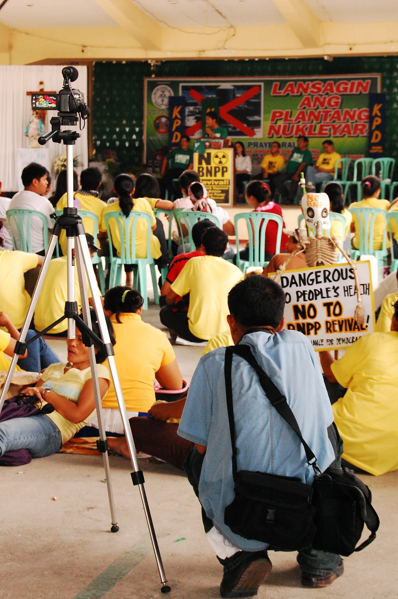 A speaker discusses the cons of the w:Bataan Nuclear Power Plant revival while being recorded on video. Amongst him are also against the plant's reopening. A skeleton toy can be seen in the photo, hinting terror and deadly danger.
This was taken in a basketball court around Morong Parish Church Compound where a Catholic mass had been held hours before.