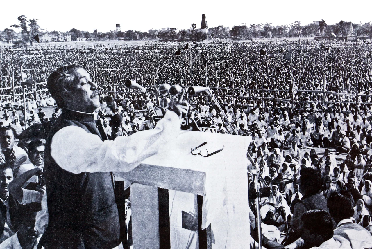 Photograph showing Sheikh Mujibur Rahman (also known as "Bangabandhu") delivering his historic speech "7 March Speech of Sheikh Mujibur Rahman" on 7 March 1971 at the then Ramna Race Course (now Suhrawardy Udyan), Dhaka, East Pakistan (now Bangladesh). The mass gathering can be seen behind him, as he raised his hand in address. This speech is widely regarded as the de-facto proclamation of Bangladesh’s struggle for independence.
